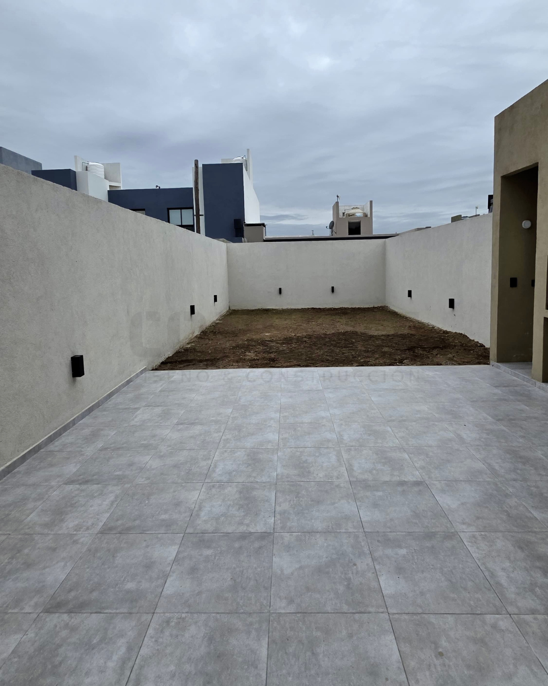 patio-trasero-am2 Patio trasero de AM2 con piso cerámico gris y muro perimetral.